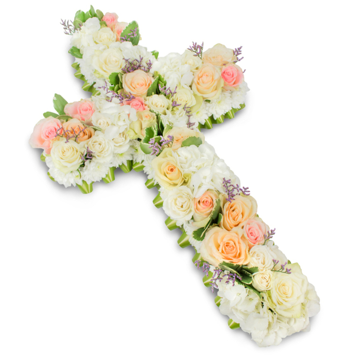 A large, meticulously arranged floral cross is presented against a pure white studio background, its gentle colours and lush texture creating a sense of quiet reverence. The entire cross is constructed from masses of fresh flowers, with a rich underlying base of white and creamy blooms that forms a thick, cushion-like surface. Ivory and white roses open gracefully across the design, their layered petals catching the light, while smaller spray roses and possibly white chrysanthemums fill in every space so that the cross appears dense and abundant. Interwoven among these pale blossoms are clusters of pastel roses in soft peach, apricot, and light blush pink, placed to create a subtle, flowing gradient that moves along the length and width of the cross. Occasional touches of lavender or pale purple filler flowers are scattered delicately throughout, adding just a whisper of colour and enhancing the visual depth without overpowering the calm, pastel theme. Slender hints of green foliage peek from beneath the blooms, tracing the smooth, rounded edges of the cross and giving it a natural, finished frame. The Christian symbol is instantly recognisable, yet softened by the generous layering of petals, suggesting tenderness and compassion. Under soft, balanced lighting, every flower head is clearly defined, revealing the careful craftsmanship and attention to detail behind the piece. This floral cross would make a respectful funeral tribute for a service in Southgate, whether placed beside the pulpit in a local church or delivered to a chapel of rest near Southgate Underground. It conveys faith, peace, and a heartfelt farewell, offering comfort to those gathered to remember a loved one.