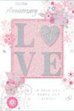 This photograph shows a refined anniversary card that feels as gentle and heartfelt as a pastel bouquet delivered to a Southgate doorstep. At its heart, the word LOVE is set in large, raised letters, each one dusted with fine glitter that shimmers in tones of blush pink, pearly white, and soft silver. The letters stand slightly proud of the card, giving a pleasing tactile sensation under the fingertips, like tracing the curve of a rose petal. Behind them, the background is a smooth blush pink, evenly lit and serene, reminiscent of the soft skies above Southgate Green in early evening. All around the central word, a graceful pattern of stylised flowers, curling vines, and decorative leaves drifts across the surface. The blooms are drawn with delicate, illustrative lines and shaded in pastel pinks and silvery greys, with occasional highlights of silver foil that catch the light subtly. The pattern has an airy, floating quality, like petals caught in a gentle breeze, suggesting both celebration and calm. In elegant script, an anniversary message is woven into the design, the lettering slender and flowing, reinforcing the card's tone of sincere affection. The overall mood is intimate and romantic, refined yet understated, much like a carefully chosen hand-tied arrangement from a trusted local florist. It's an ideal paper keepsake to accompany a soft, romantic bouquet for a special anniversary evening in Southgate.